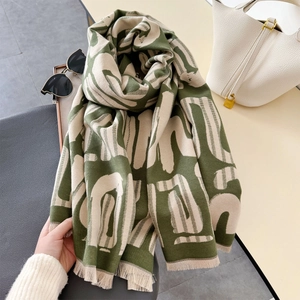 Dettaglio di morbida sciarpa verde e beige con frange sottili e motivi astratti