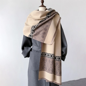 Detailed view of bohemian knit shawl with geometric patterns and fringe on wool coat
