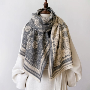 Grau-weißer Paschmina-Schal mit Paisley-Muster und Quasten über einem eleganten Wintermantel