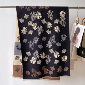 Detail of a thick black scarf with beige ginkgo leaf prints and fine fringe edges