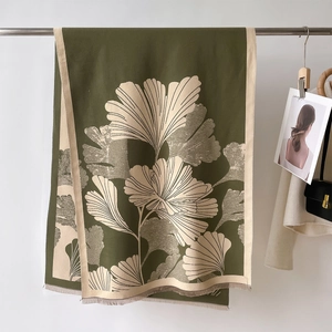 Detail of olive green scarf featuring beige ginkgo leaf patterns and fringe tassels