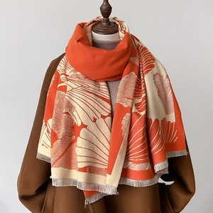 Thick winter scarf with orange and cream leaf pattern and tassels on mannequin