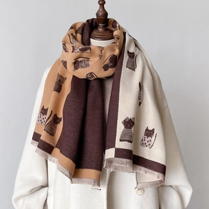 Detail eines Winterschals mit Katzenmotiven und Fransen auf einem weißen Wollmantel