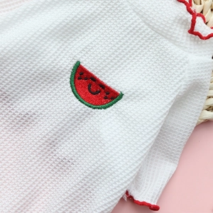 Gros plan d'un t-shirt gaufré blanc pour animaux avec bords ondulés rouges et broderie pastèque
