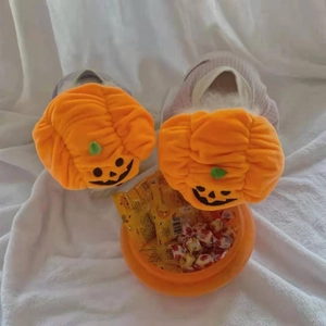 Close-up of orange plush pumpkin slippers with embroidered faces and green leaf details