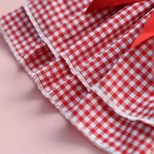 Detail of red and white plaid dog dress with multi-layer ruffles and red satin bow