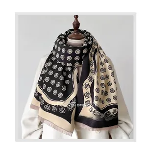 Détail du motif camélia et des franges sur cette écharpe en cachemire noir et beige