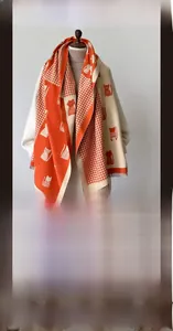 Detail of warm orange and beige cat print scarf with tassel trim and houndstooth pattern