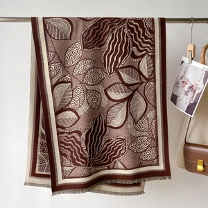 Thick faux cashmere scarf with leaf pattern and tassels displayed on metal rack