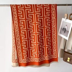 Detail view of orange knit shawl with beige Greek key patterns and fringe edges