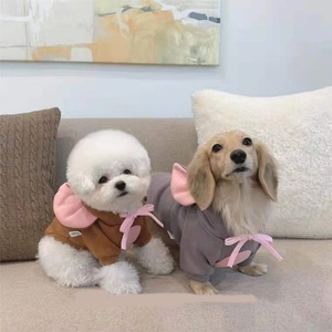 Detail of warm brown and grey fleece pet hoodies with pink bows on dogs in a home setting