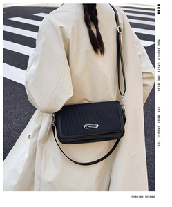 Close-up of black retro crossbody bag with textured flap and FASHION metal plaque