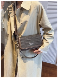 Detailed close-up of brown crossbody bag with woven texture and silver metal fashion plaque