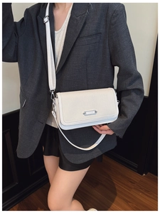 Close-up of white crossbody bag with woven texture and silver hardware on a grey blazer
