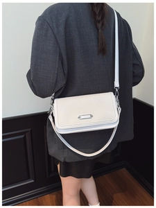 Close-up of white crossbody bag with woven texture and silver buckle on a gray blazer
