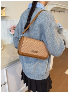 Close-up of woven crossbody bag featuring brown leather trim and fashion metal plaque