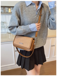 Detail view of brown crossbody bag with woven texture and fashion metal plaque on front