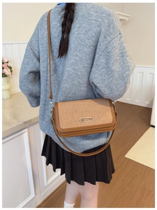 Close-up of brown woven crossbody bag with silver FASHION plaque worn over a grey sweater
