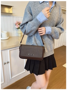 Detail of vintage brown shoulder bag featuring woven texture and fashion metal plaque