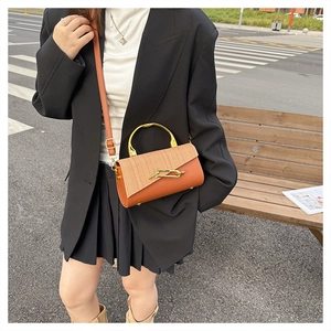 Outdoor shot of stylish PU leather crossbody bag with woven flap and golden metal handle