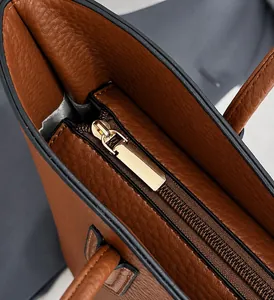 Macro shot of smooth gold zipper and lychee pattern leather on dark brown bucket bag