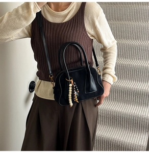 Detail of black Boston bag with dual handles and vintage wooden bead charm accessory