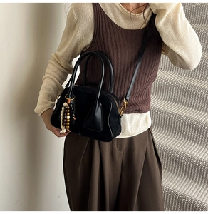 Detail of matte black Boston bag with wooden bead tassel and elegant top handles