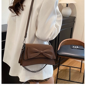 Dettaglio di una borsa a tracolla marrone in pelle opaca con fiocco decorativo e tracolla a catena