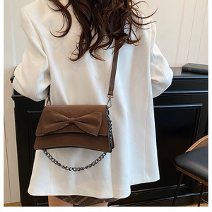 Dettaglio borsa a catena marrone con fiocco decorativo su sfondo blazer bianco chic