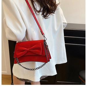 Dettaglio borsa rossa con fiocco e catena argentata indossata su blazer bianco