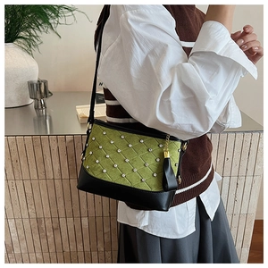 Close-up of quilted green suede bag with diamond accents, black trim, and fringe detail