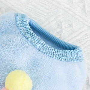 Dettaglio del gilet in pile azzurro per animali con scollo a costine e pompon giallo decorativo