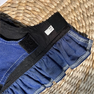 Close-up of denim pet harness with ruffle trim and size XS label on woven straw mat