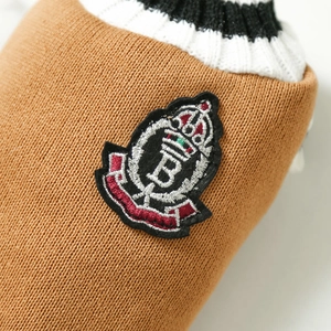 Detail of camel knit pet vest showing preppy crest embroidery and striped ribbed edges