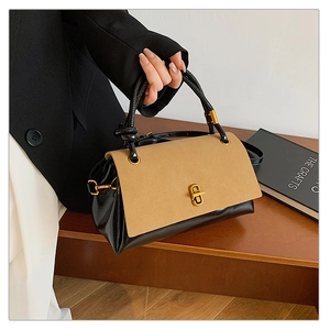 Detail of suede patchwork handbag featuring a gold twist lock and black knotted handle