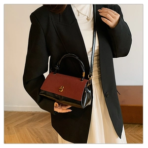 Detail of burgundy suede and black leather bag with gold clasp and elegant wood background