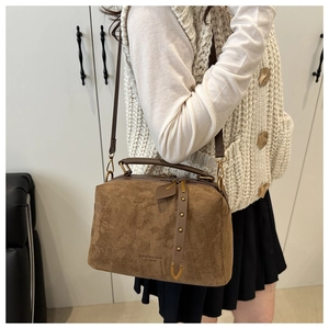 Détail du sac polochon en daim marron avec coins métalliques et lettrage embossé