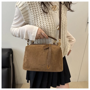 Détail du sac polochon en daim marron avec rivets vintage et lettrage gravé à la mode