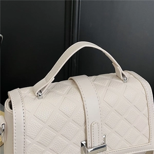 Detail of beige quilted leather texture and polished silver metal clasp on the handbag