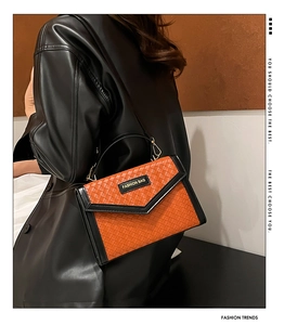 Close-up of woven crossbody bag showing orange texture, black leather trim and metal logo