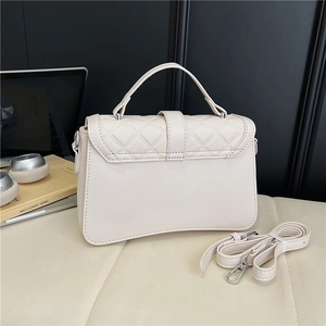 Detail of cream quilted handbag featuring a top handle and adjustable silver hardware strap
