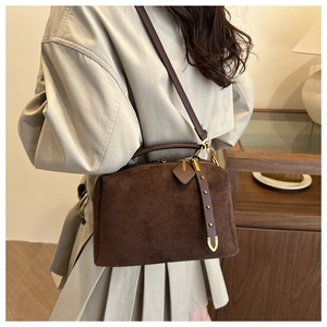 Détail du sac polochon en daim marron foncé avec rivets dorés et texture cuir mat
