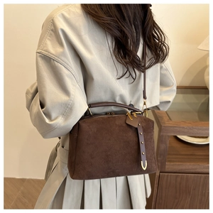 Détail du sac boston en daim marron foncé avec poignées en cuir et garniture dorée chic
