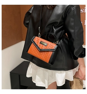 Detail of woven crossbody bag in orange and black with metal fashion bag logo plate