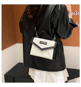 Detail of woven crossbody bag with black leather trim and 'FASHION BAG' plaque
