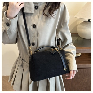 Détail du sac polochon en daim noir avec logo doré et bandoulière en cuir réglable