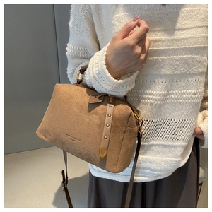Détail du sac Boston en daim marron avec rivets dorés et poignée en cuir porté avec pull