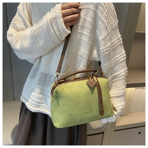 Détail du sac boston en daim vert vif avec poignées en cuir marron et rivets décor