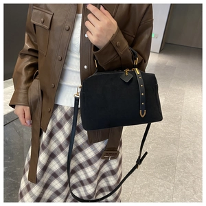 Détail du sac bandoulière en suédine noire avec rivets dorés porté par un mannequin