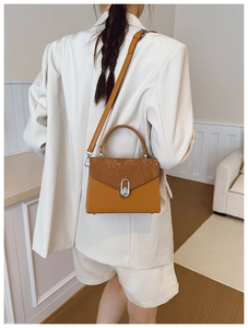 Close-up of structured mustard yellow handbag with snake print flap and silver twist lock